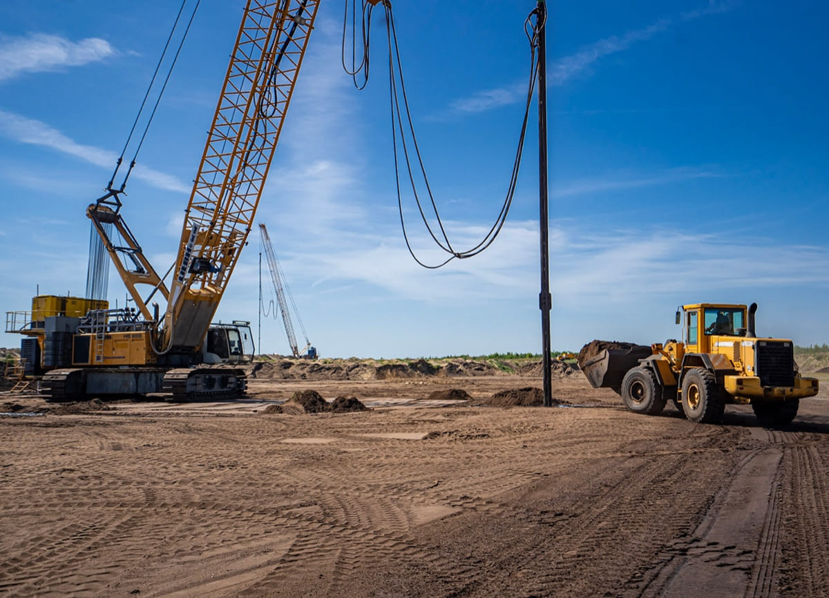 Baustelle im ehemaligen Tagebau: ein Seilbagger und ein Radlader auf verdichtetem Sandboden unter blauem Himmel